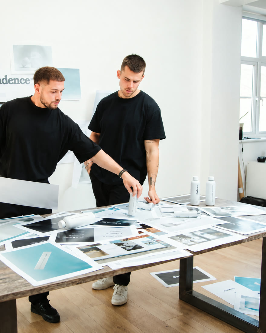 Two designers in black T-shirts reviewing prints spread across a table