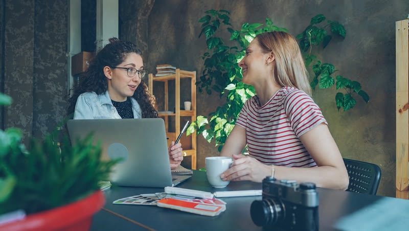 Two colleagues talking over coffee at a table, the white Larkin band on one woman’s wrist